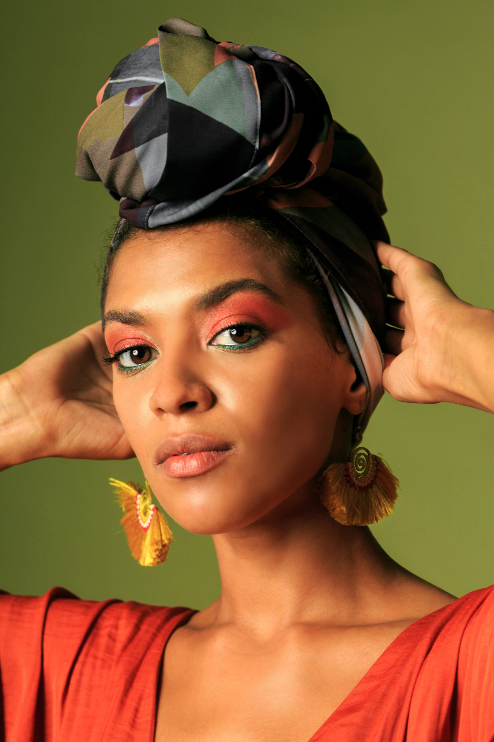 Black African American woman in  orange clothing and ethnic head wrap  i poing in studio. Bright make up.