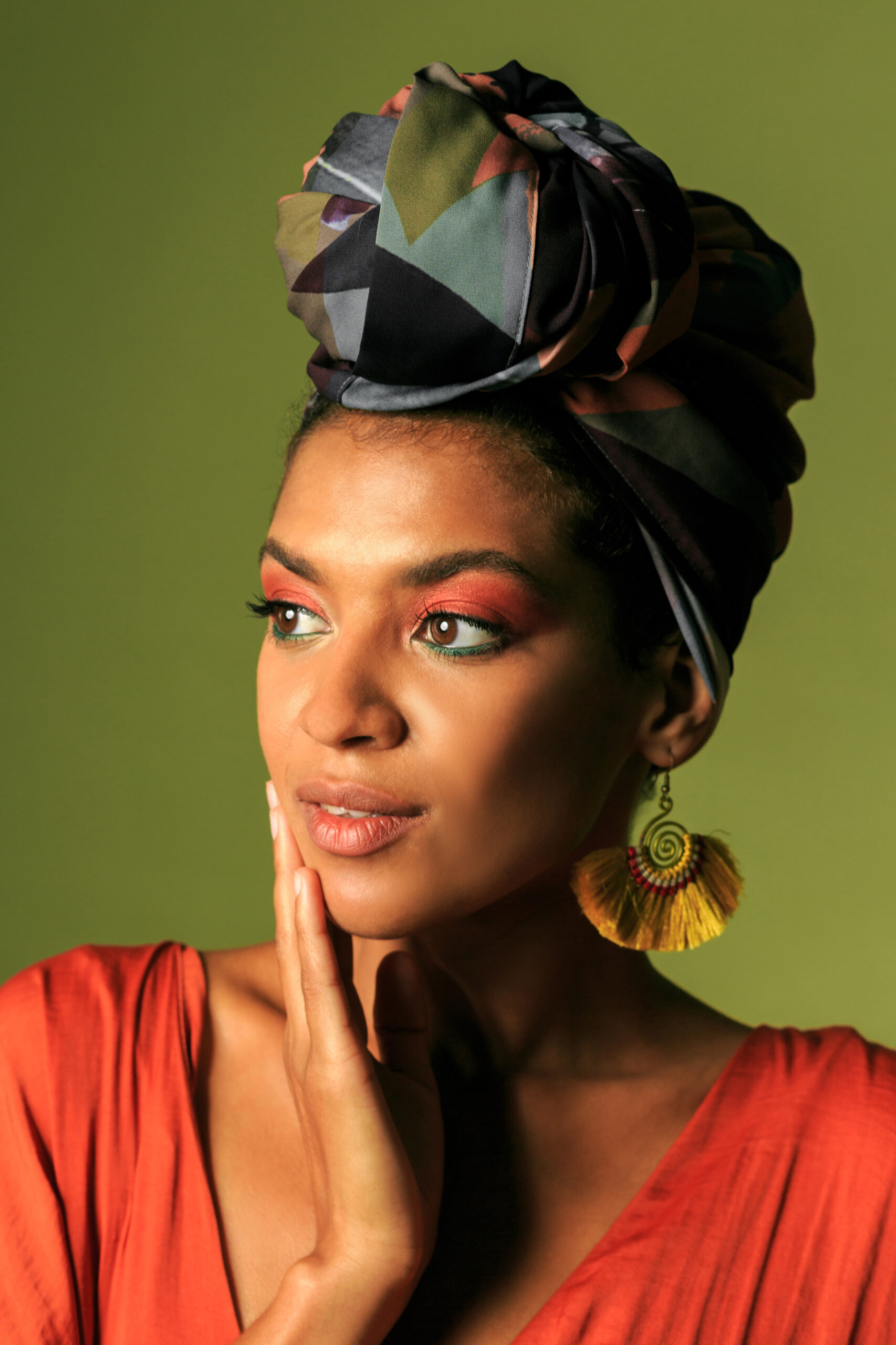 Stylish african  woman with  colorful turban in studio. Beautiful female model with vibrant makeup against  green background.